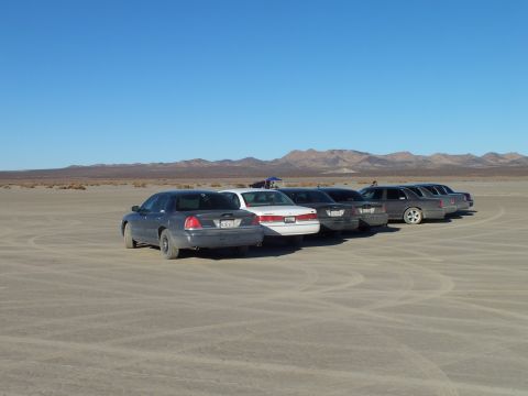 2003 Ford Crown Victoria - Full-size sedans and a wagon staged on a lakebed under blue sky