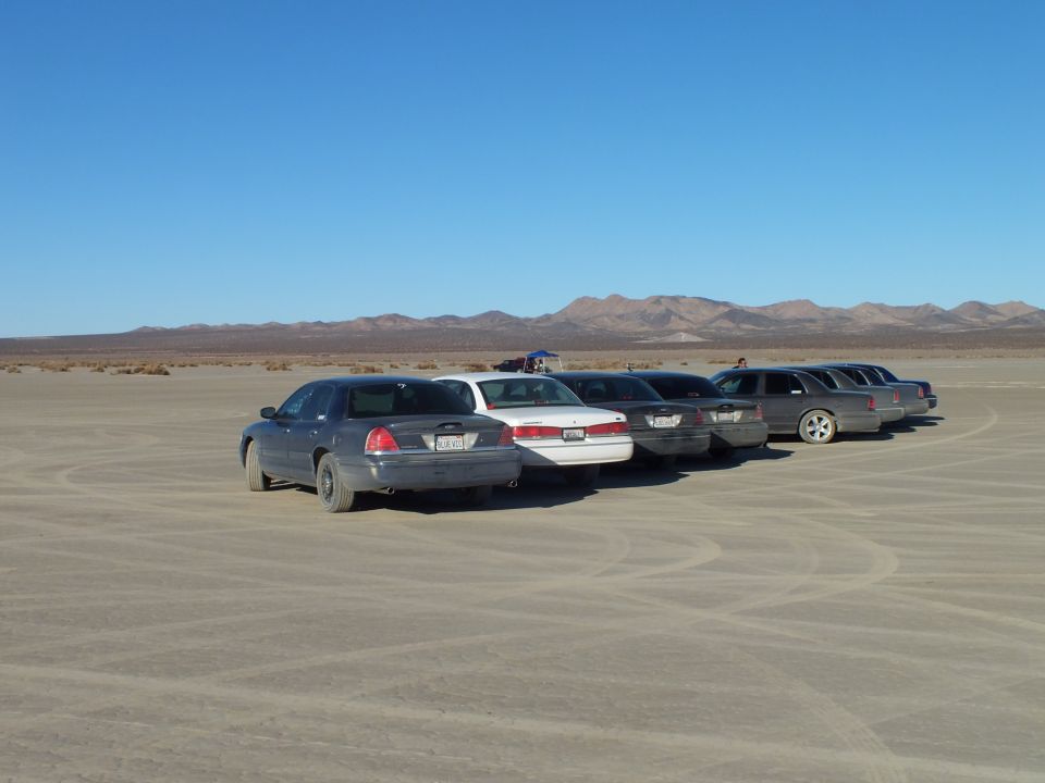 Sedans and wagons parked in a row on cracked desert ground
