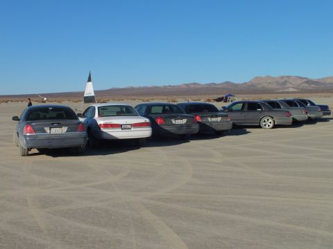 2003 Ford Crown Victoria - Lineup of sedans and wagons on desert hardpan beside a pointed marker