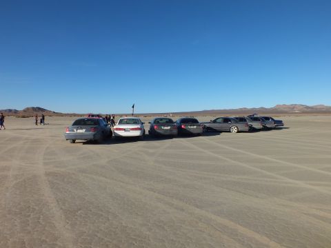 2003 Ford Crown Victoria - Car meet on desert playa with sedans, wagons and onlookers at left