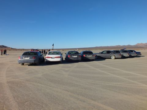 2003 Ford Crown Victoria - Row of full-size sedans and wagons on hardpan with a flag and crowd