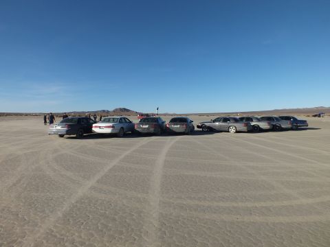 2003 Ford Crown Victoria - Sedans and wagons lined up on playa with people and a flag in distance