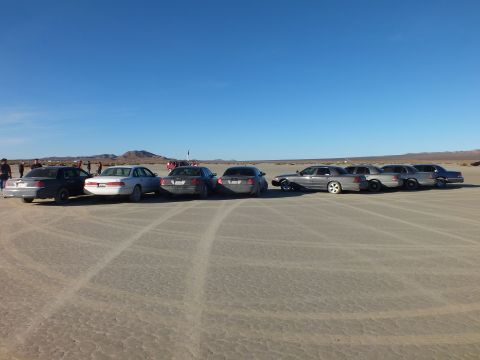 2003 Ford Crown Victoria - Full lineup of full-size sedans and wagons on dry playa with crowd at left
