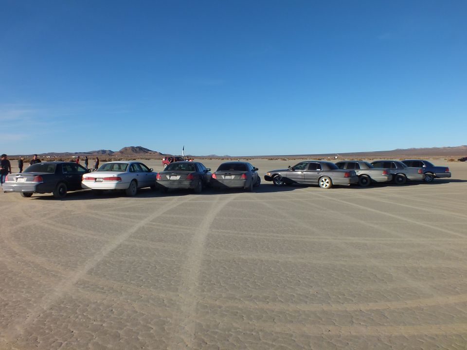 Sedans and wagons parked in a long row on a desert lakebed