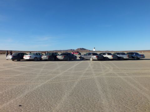 2003 Ford Crown Victoria - Sedans and wagons staged across playa beside a pointed obelisk marker