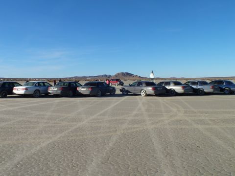 2003 Ford Crown Victoria - Sedans and wagons lined up on hardpan with mountains and a marker behind