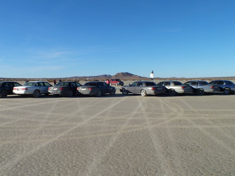 Row of full-size sedans and wagons on a desert lakebed at low sun
