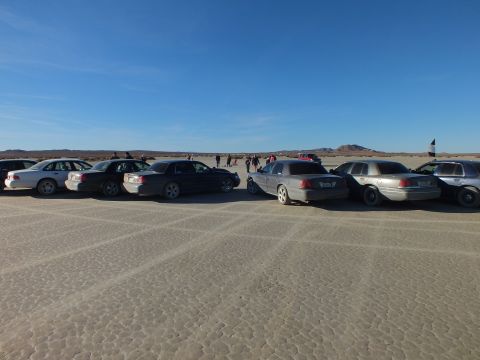 2003 Ford Crown Victoria - Full-size sedans staged in opposing rows on playa with crowd in distance