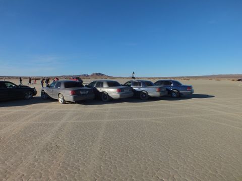 2003 Ford Crown Victoria - Lineup of full-size sedans on hardpan with a flag and crowd behind