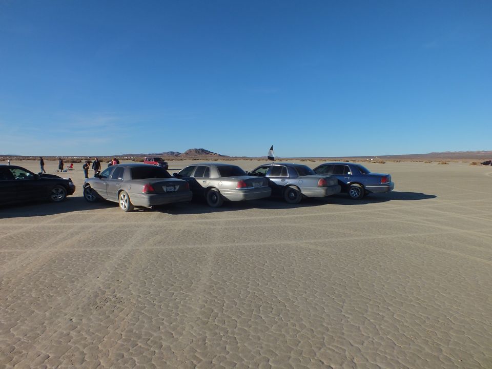 Silver and gray sedans parked in a row on a dry lakebed at golden hour
