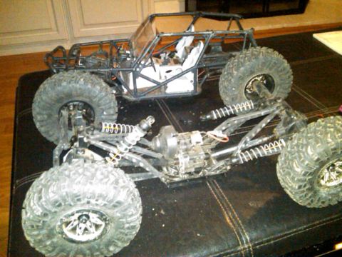 1986 Ford Bronco - Two RC rock crawlers are shown, one assembled and one partially disassembled, on a dark surface.