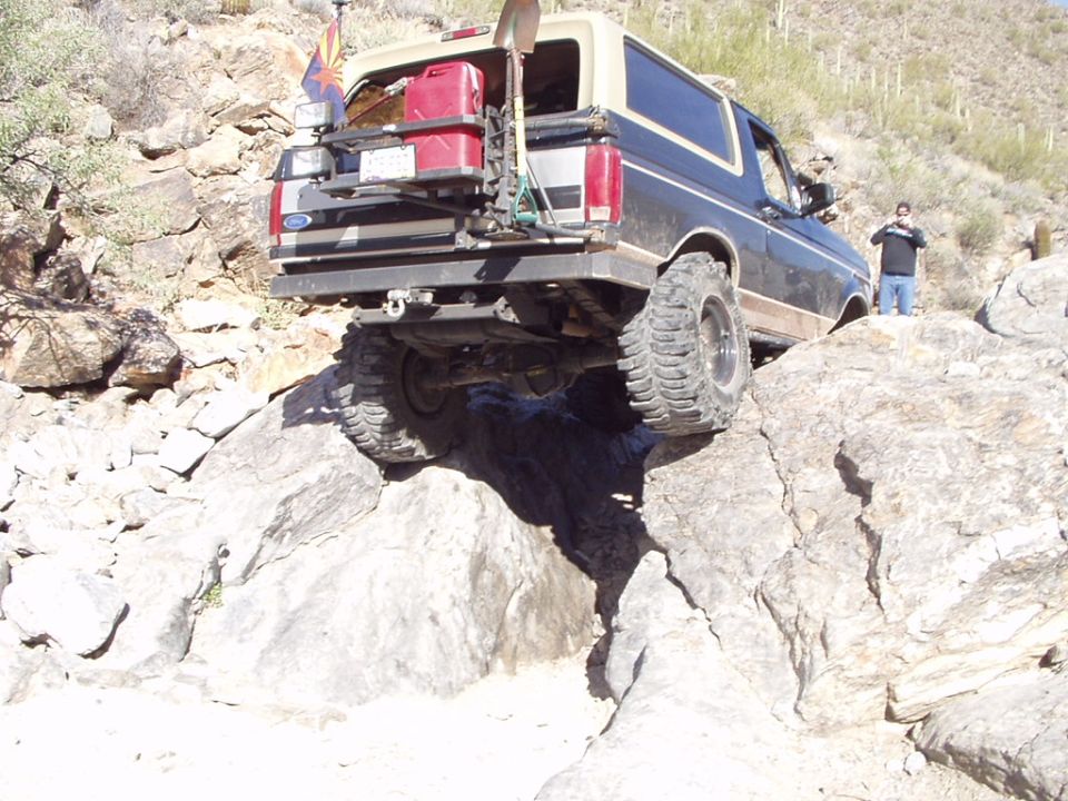 Rear view of lifted two-tone Ford Bronco crawling over boulders on a desert trail