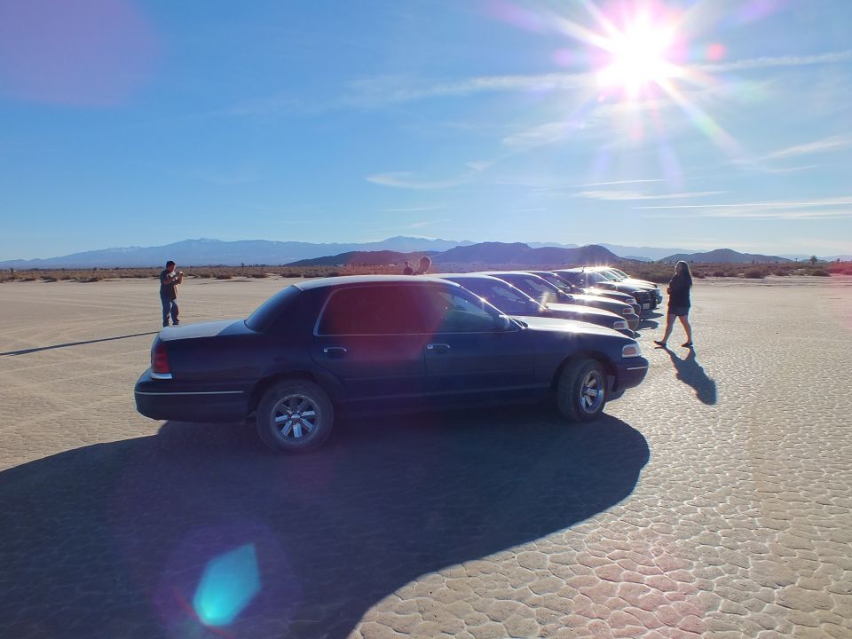Dark blue Crown Victoria leading a row of sedans on lakebed with bright sun burst