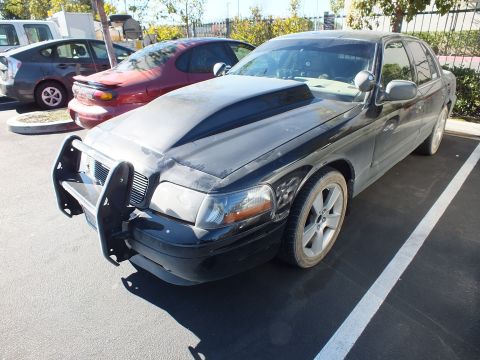 2003 Ford Crown Victoria - Front three-quarter of a dark Panther sedan with grille guard and alloy wheels in a parking lot.