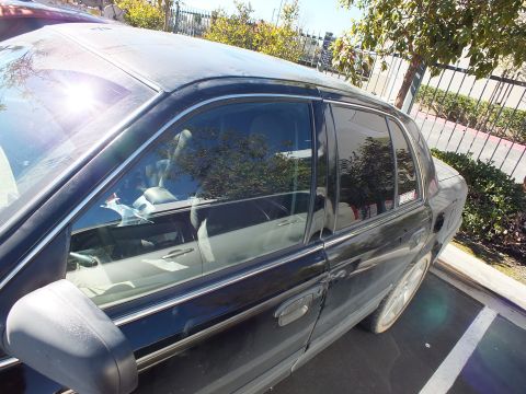 2003 Ford Crown Victoria - Sun flares off the tinted rear side glass of a dark sedan parked beside a wrought-iron fence.