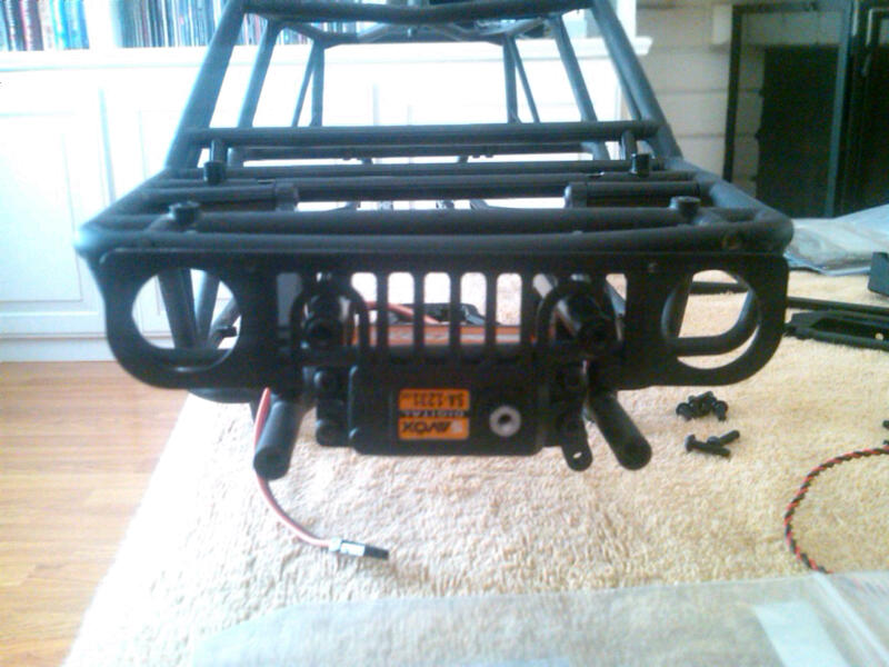 RC car chassis front with black roll cage and a black servo motor with orange label