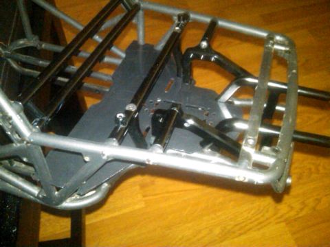 1986 Ford Bronco - The chassis of a remote-controlled car is shown, a complex arrangement of metal tubing and suspension parts.