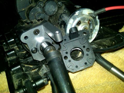 1986 Ford Bronco - Close-up of RC car drivetrain parts, including a motor mount and driveshaft, with a red wire visible.