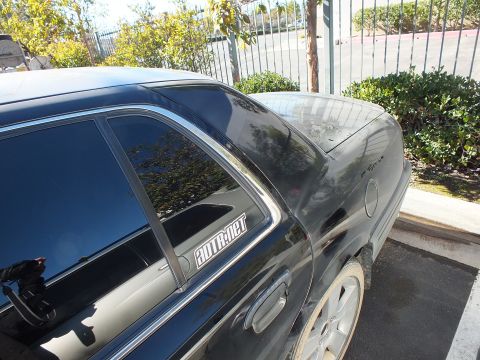 2003 Ford Crown Victoria - Rear quarter glass and trunk of a black sedan with alloy wheel and a SuperMotors watermark.