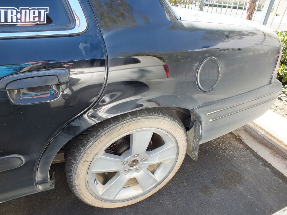 Black sedan rear quarter panel, fuel door and silver alloy wheel close-up