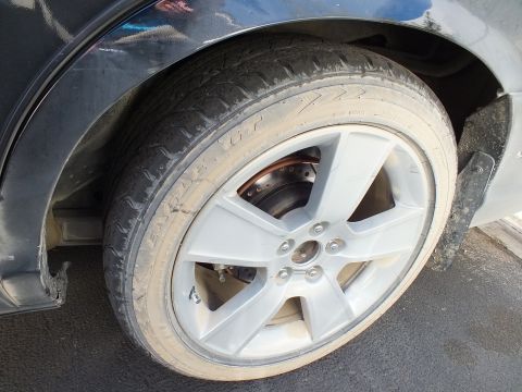 2003 Ford Crown Victoria - Detail of a dirty silver five-spoke alloy wheel mounted on a dark car.