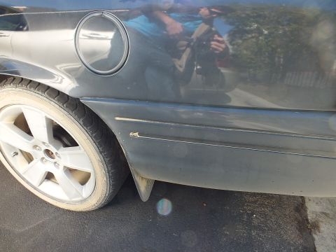 2003 Ford Crown Victoria - dark sedan's body panel reflects the photographer near the fuel door and alloy wheel.
