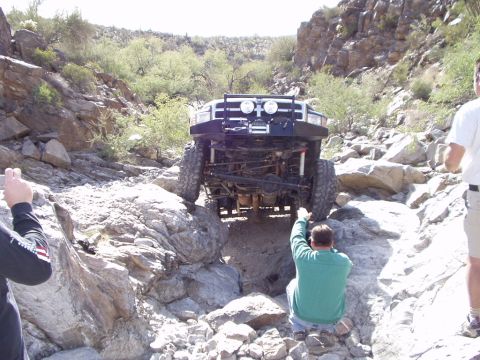 1993 Ford Bronco - A 1993 Ford Bronco is driven over large rocks in a desert canyon, with people observing the off-road maneuver.