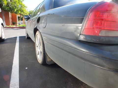 2003 Ford Crown Victoria - Low rear-quarter view of a dark Crown Victoria with alloy wheel in a marked parking stall.