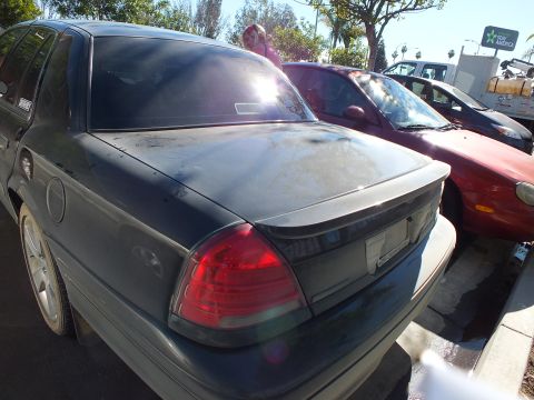 2003 Ford Crown Victoria - Rear of a faded dark Crown Victoria parked next to a maroon sedan and a truck.