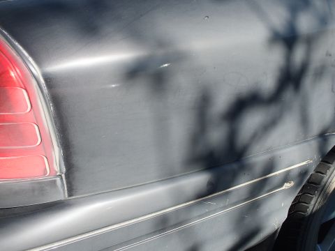 2003 Ford Crown Victoria - Detail of a dark sedan's rear quarter panel with red tail lens and chrome rocker molding.