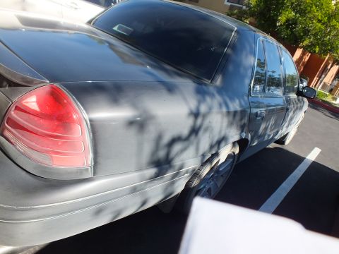 2003 Ford Crown Victoria - Rear three-quarter of a dark Crown Victoria sedan with sun glare across the roof.
