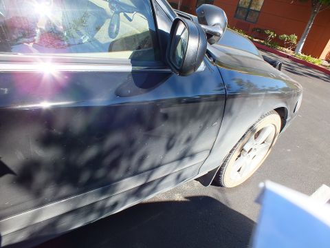 2003 Ford Crown Victoria - Sun flares through the glass of a dark sedan's front door beside the side mirror and wheel.
