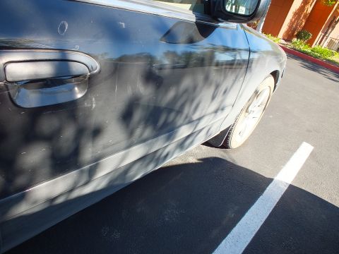 2003 Ford Crown Victoria - Front door handle, fender and alloy wheel of a dark sedan in a striped parking space.