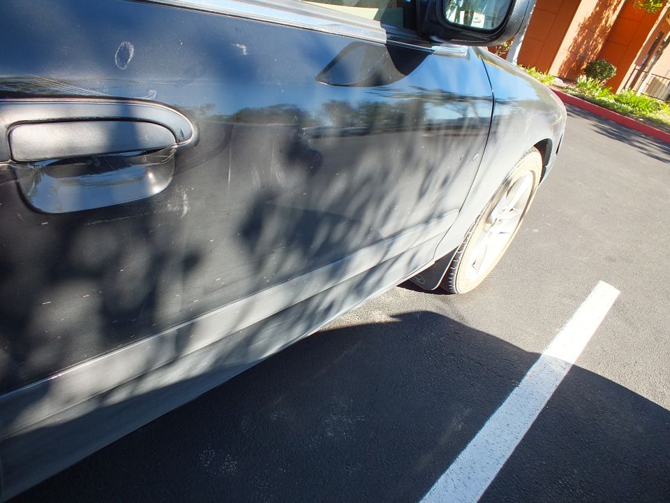 Dark sedan front door handle, fender and alloy wheel in a parking lot