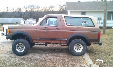 1987 Ford Bronco - This lifted 1987 Ford Bronco is parked on a gravel surface next to a curb, with houses in the background.