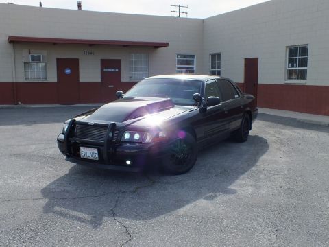 2003 Ford Crown Victoria - Black Crown Victoria Police Interceptor with brush guard parked outside a commercial building.