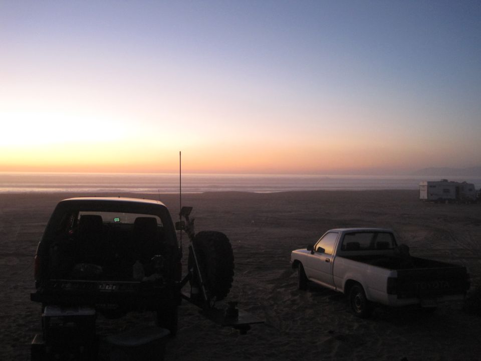 Two trucks and RVs on a sandy beach during sunset