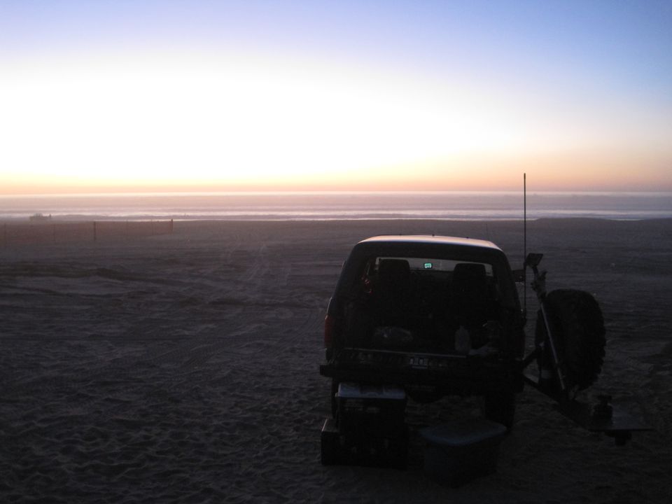 SUV parked on a sandy beach with the ocean and sunset in the background