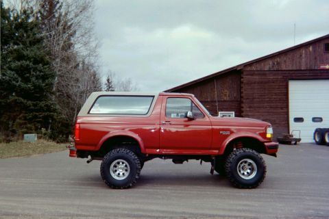 1995 Ford Bronco - This lifted Ford Bronco, likely from the early to mid-1990s, is shown from the side in front of a large wooden structure.
