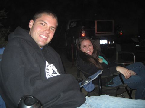 1989 Ford Bronco - Two people relax in camping chairs at night, with a dark SUV visible behind them.