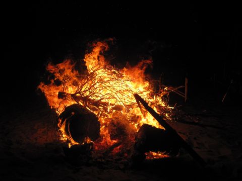 1989 Ford Bronco - A large bonfire burns brightly against the dark night sky, illuminating logs and branches.