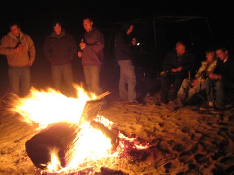 1989 Ford Bronco - Friends enjoy a nighttime bonfire on the sand, holding drinks and conversing.