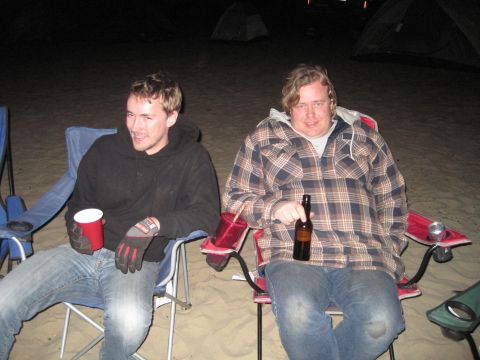 1989 Ford Bronco - Two men relax in camping chairs on a sandy area at night, with tents visible in the background.