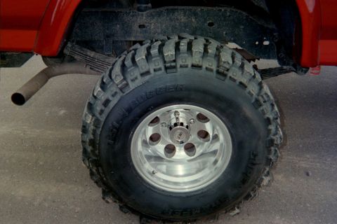 1995 Ford Bronco - Close-up of the rear tire and suspension of a red 1995 Ford Bronco, aggressive off-road tires.