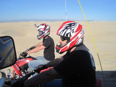 1989 Ford Bronco - Two individuals ride ATVs through a sandy desert landscape under a clear blue sky.