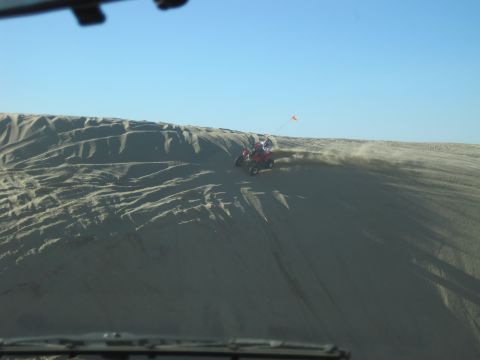 1989 Ford Bronco - An ATV rides down a sandy dune under a clear blue sky.