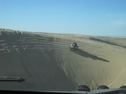 1989 Ford Bronco - Quad bike navigates sand dunes on a sunny day, seen from another vehicle's perspective.