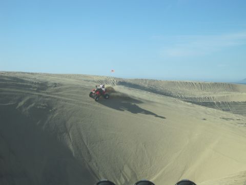 1989 Ford Bronco - An ATV rides up a sand dune, kicking up a cloud of sand under a clear blue sky.