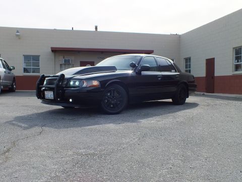 2003 Ford Crown Victoria - Black Police Interceptor sedan front quarter view, grille guard and dark tint, overcast lot.