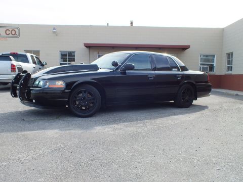 2003 Ford Crown Victoria - Black Police Interceptor with push bumper and dark tint angled toward camera in a paved lot.